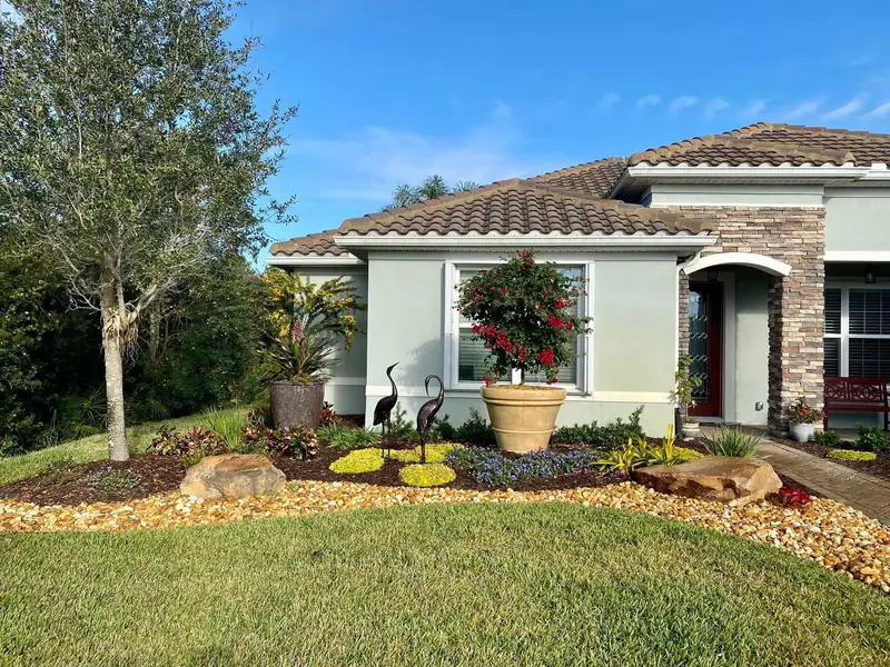 Front yard with a river-rock-edged bed, two boulders, crane statues and a bougainvillea standard in a large urn, by The Master’s Touch Landscape and Design