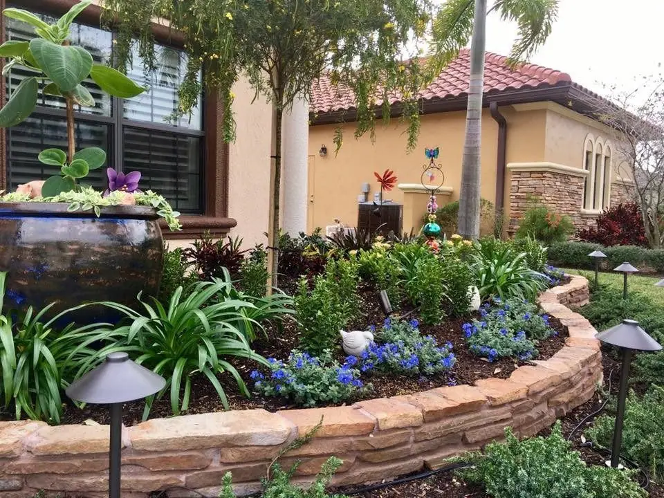 Low stacked-stone wall curving around a planted bed with path lights at a tile-roofed home in Melbourne, by The Master’s Touch Landscape and Design