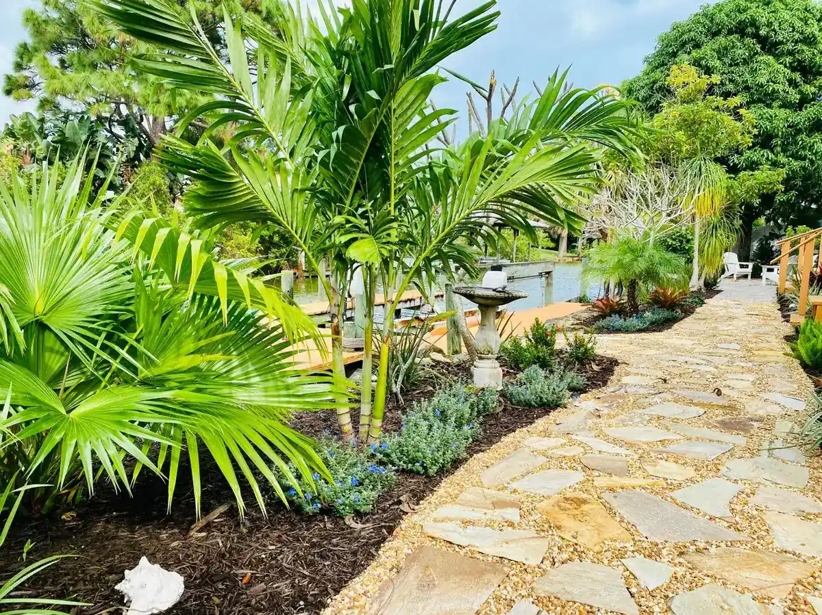 Flagstone path set in gravel through palms and tropical beds in a canal-front backyard on Merritt Island, by The Master’s Touch Landscape and Design