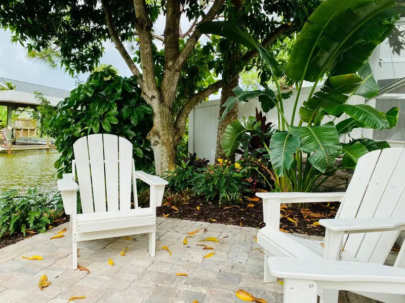 Paver patio with white Adirondack chairs under a shade tree beside a canal on Merritt Island, by The Master’s Touch Landscape and Design